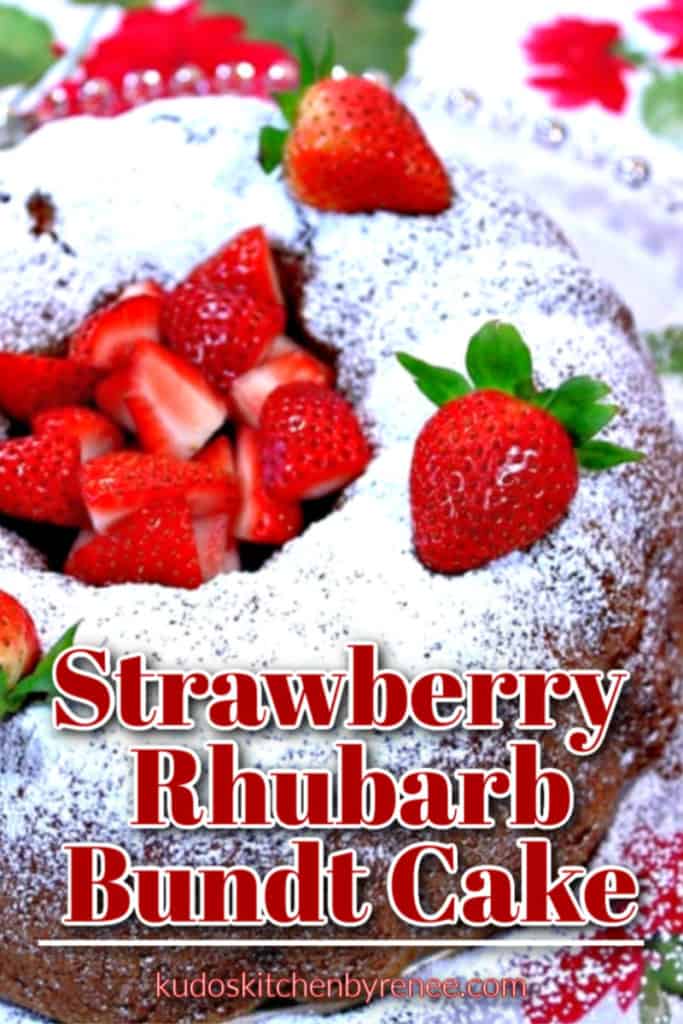 Closeup title text overlay image of a strawberry rhubarb bundt cake with fresh strawberries is the middle and a confectioners sugar dusting on top.