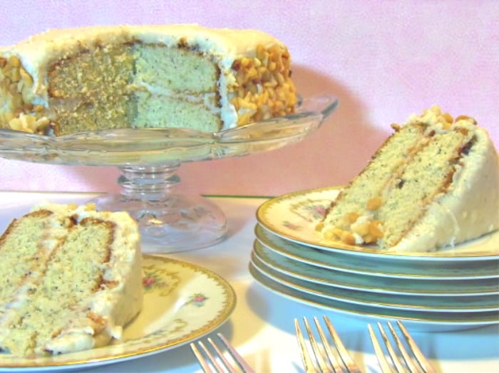 A banana poppy seed cake on a glass cake stand with two slices of cake on plates with a pink background.