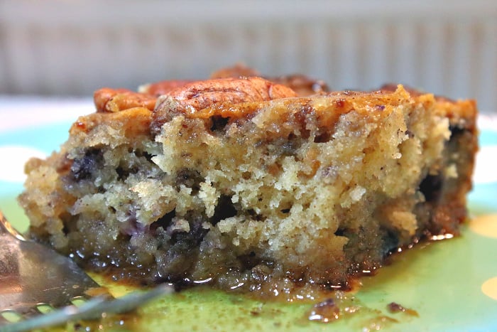 An extreme closeup of a slice of sausage blueberry breakfast casserole with a fork and maple syrup.