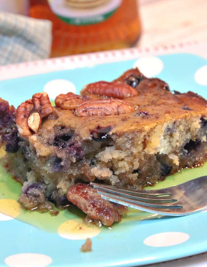 A closeup vertical image of a sausage blueberry breakfast cake square on a blue polka dot plate with pecans and maple syrup.