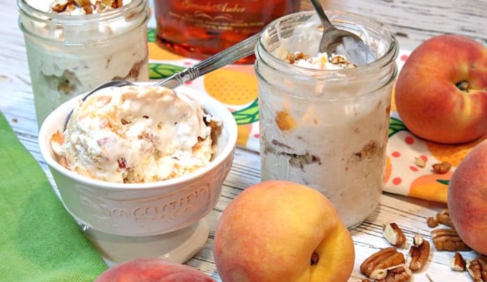 A bowl and a couple of mason jars filled with no-churn peach and pecan ice cream with peaches on the side and pecans on the table