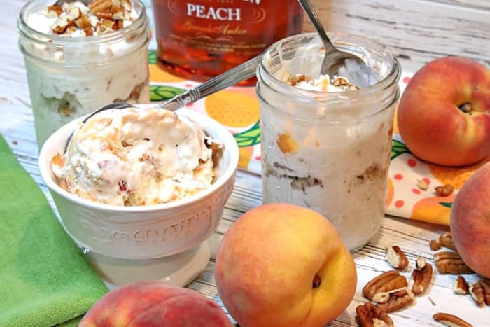 A bowl and a couple of mason jars filled with no-churn peach and pecan ice cream with peaches on the side and pecans on the table