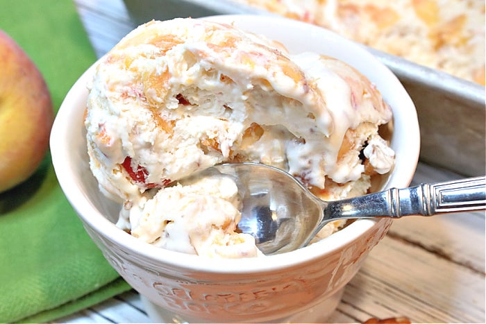 A closeup photo of a dish of no churn peach and pecan ice cream with a spoon.