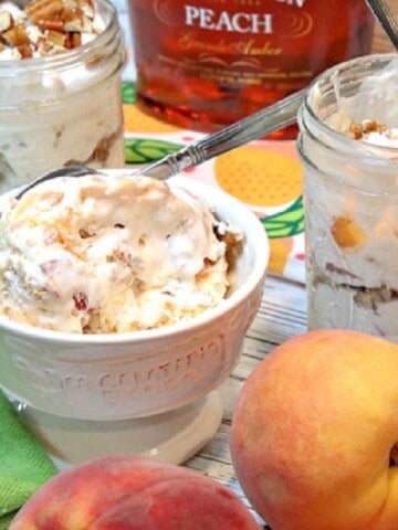 A dish of No-Churn Peach Pecan Ice Cream with fresh peaches and brandy in the background.