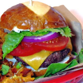 A ground short rib burger with melted cheese, tomato, red onion, and lettuce on a pretzel bun