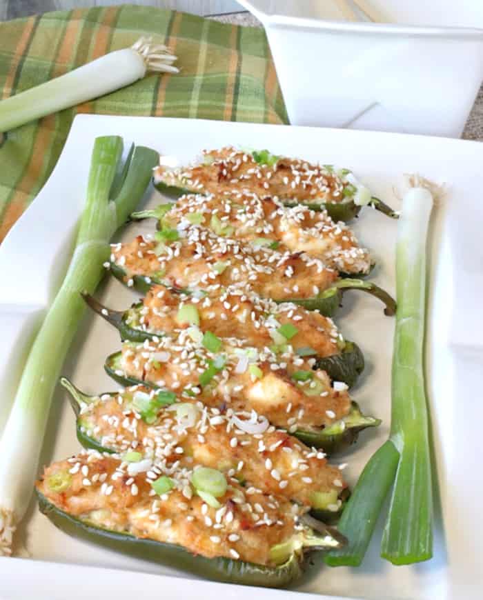 A closeup vertical photo of a white rectangle plate filled with jalapeno poppers stuffed with crab rangoon with scallions on the side of the plate.