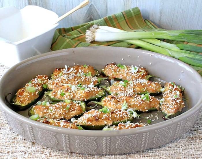 An oval tan dish filled with jalapeno poppers stuffed with crab rangoon and topped with chopped scallions