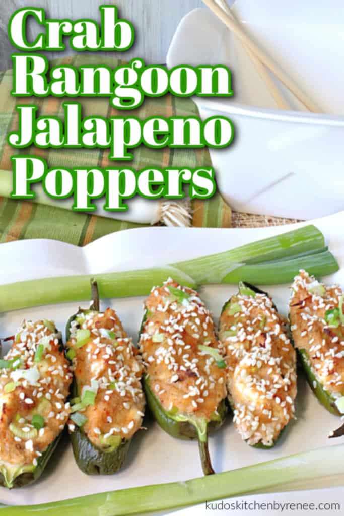 A closeup vertical photo of jalapeno poppers stuffed with crab rangoon on a white platter with chopped scallions and sesame seeds as garnish and a title text overlay graphic. How to make jalapeno poppers stuffed with crab rangoon recipe