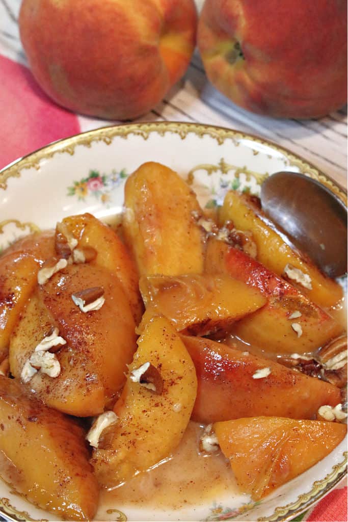 A closeup vertical image of peaches foster in a pretty china bowl  sprinkled with chopped pecans and cinnamon.