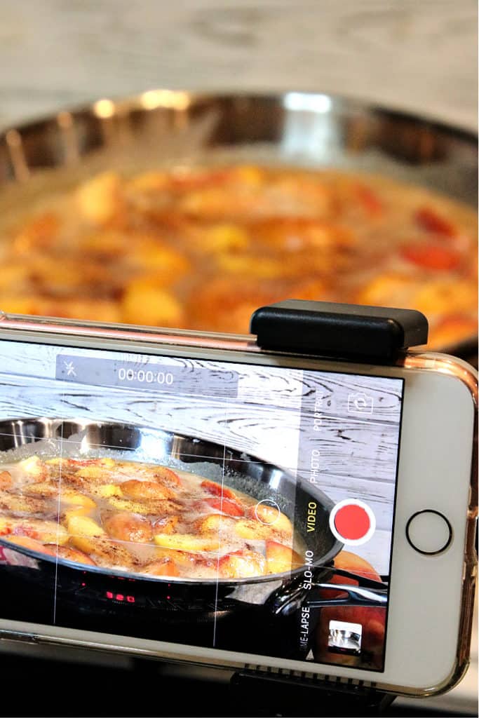 A vertical photo of an iphone taking a video of peaches foster in a silver skillet.