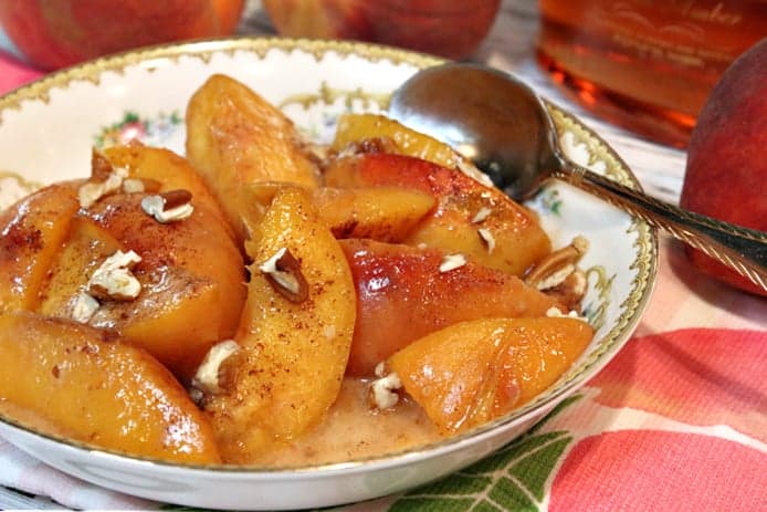 An offset photo of a bowl filled with peaches foster with chopped pecans over top.