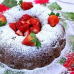 A pretty Strawberry Rhubarb Bundt Cake on a glass platter with a dusting of powdered sugar.
