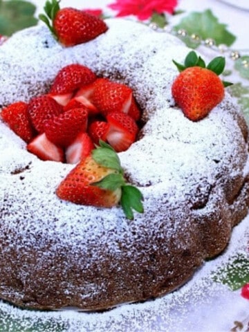 A pretty Strawberry Rhubarb Bundt Cake on a glass platter with a dusting of powdered sugar.
