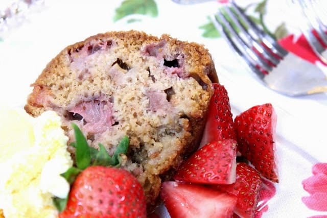 A closeup slice of strawberry rhubarb bundt cake on a plate with fresh strawberries and vanilla ice cream.