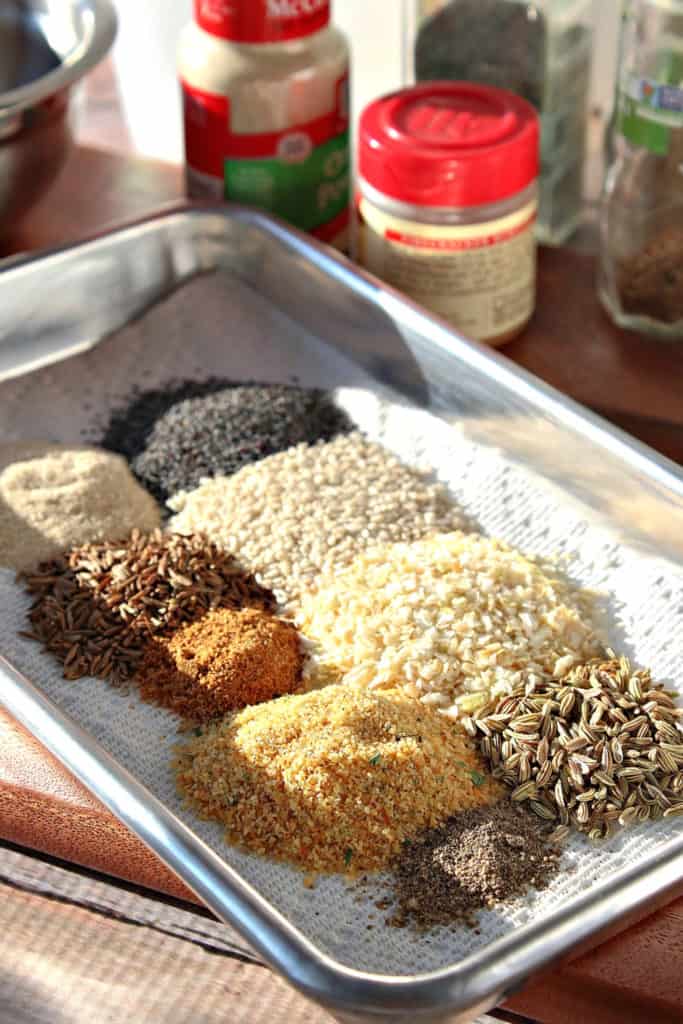 A vertical closeup image of a small baking tray filled with spices and seeds for homemade everything seasoning blend