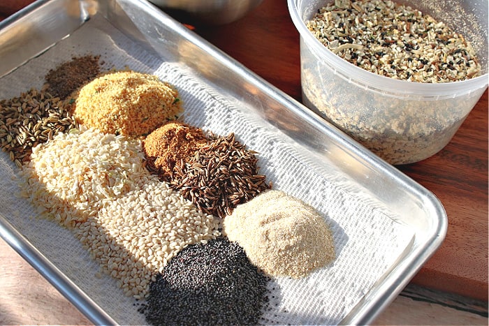 A small silver baking tray lined with a paper towel and piles of spices and seasoning for making homemade everything seasoning blend.