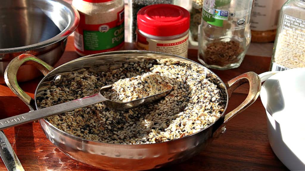 A shiny bowl filled with best everything seasoning blend along with a measuring spoon and jars of spices in the background