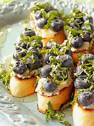 A light blue platter filled with Blueberry Basil Bruschetta topped with honey.