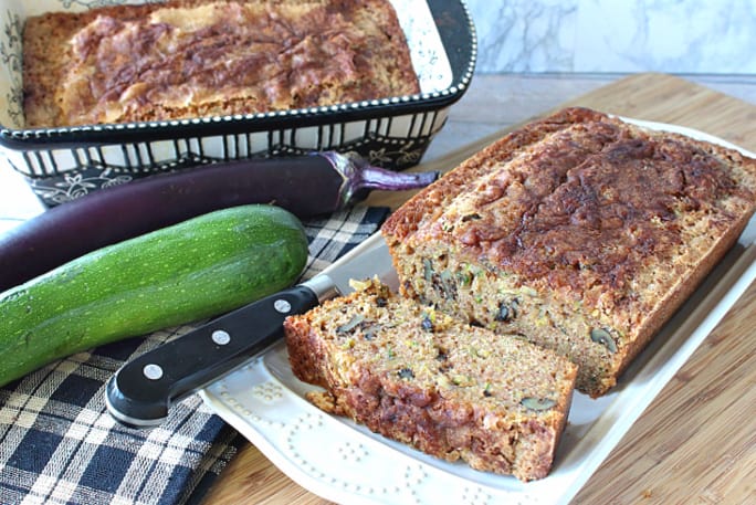 Two loaves of Eggplant Zucchini Bread with a knife, an eggplant, and a zucchini, in the background.