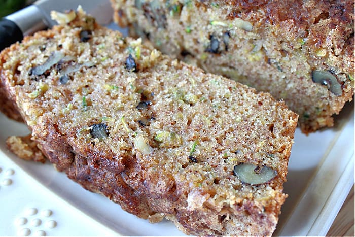 A closeup image of a slice of eggplant zucchini bread on a white plate with pieces of walnut inside.