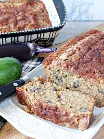 A loaf of Eggplant Zucchini Bread on a plate with a loaf pan in the background.
