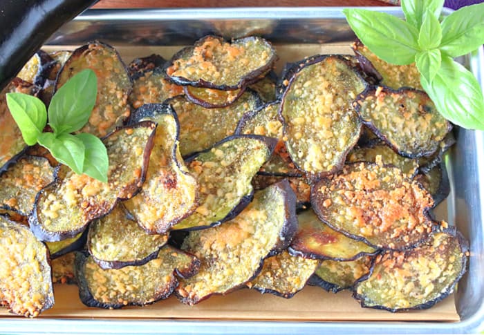 A direct overhead closeup photo of a  tray of eggplant snack chips with Parmesan cheese and fresh basil al garnish