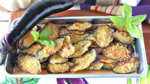 A rimmed baking sheet piled high with baked eggplant chips and topped with fresh basil.
