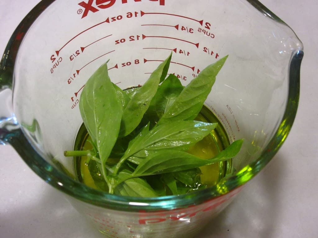 Fresh basil and olive oil in a glass measuring cup.