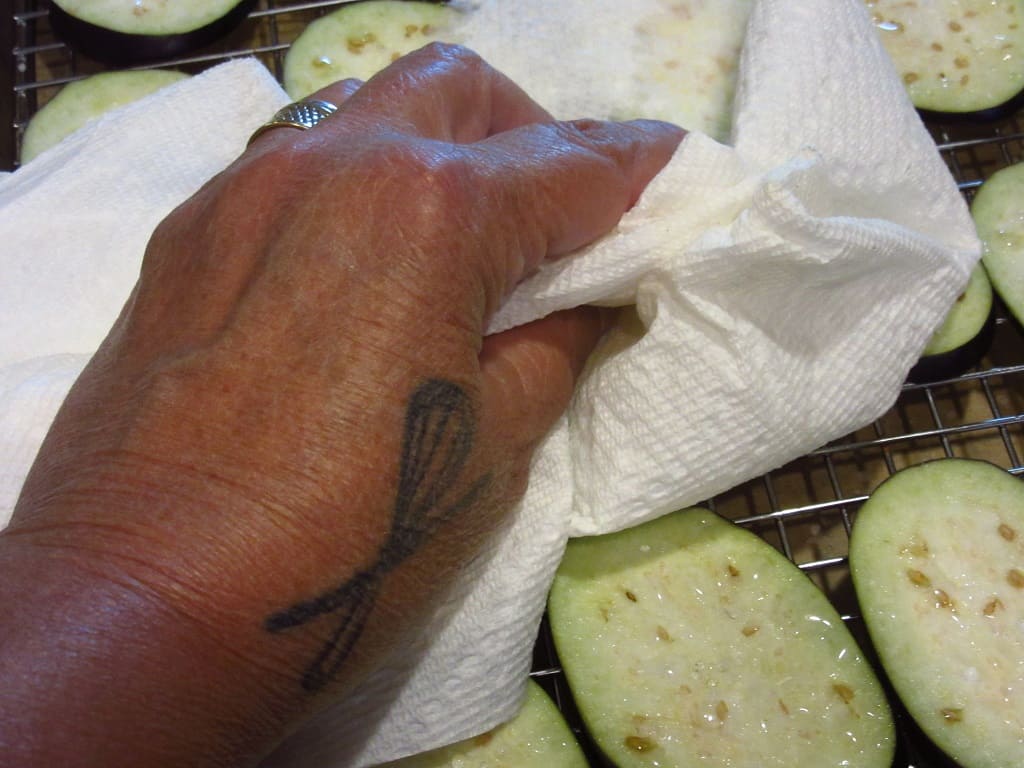 A hand with paper towels drying off eggplant slices.