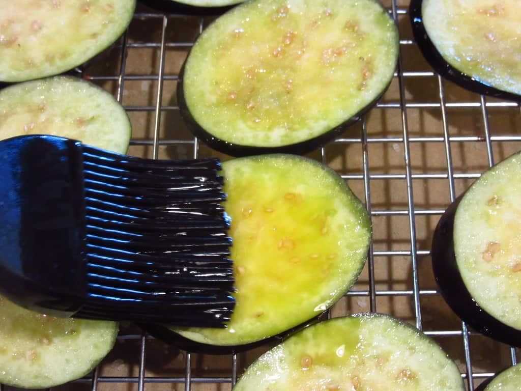 A pastry brush brushing olive oil on to eggplant slices.
