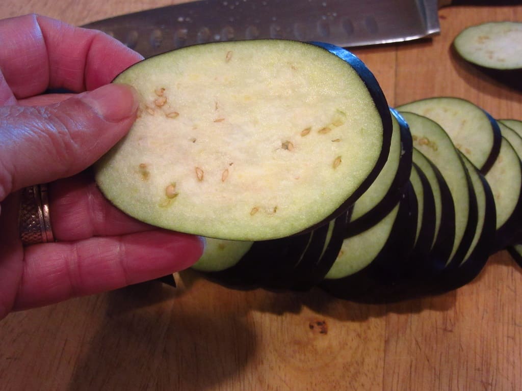 A hand holding a slice of eggplant.