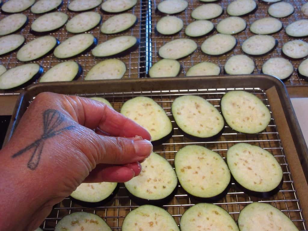 A hand sprinkling salt over eggplant slices.