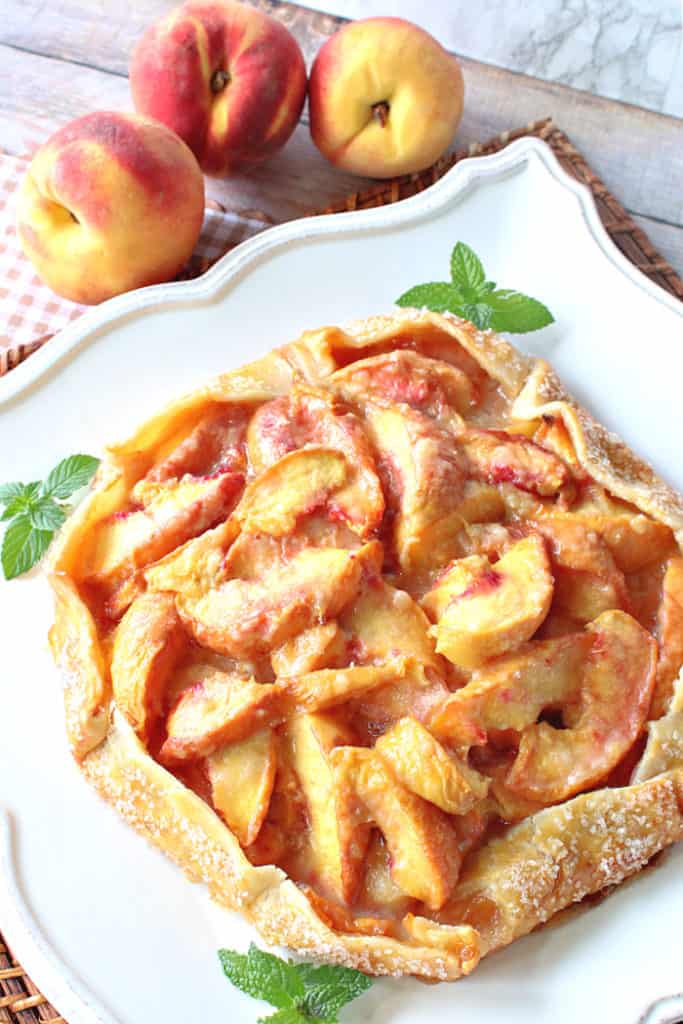 A vertical overhead closeup image of a fresh peach crostata with mint and sanding sugar as garnish.