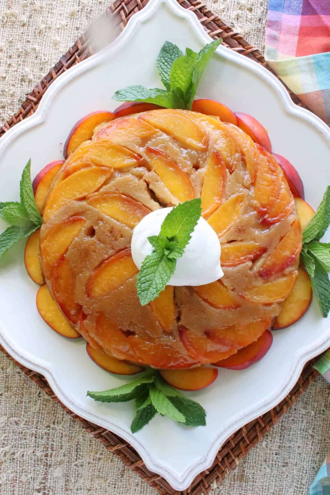 A pretty square plate with a Nectarine Upside Down Cake, whipped cream and fresh mint as garnish.