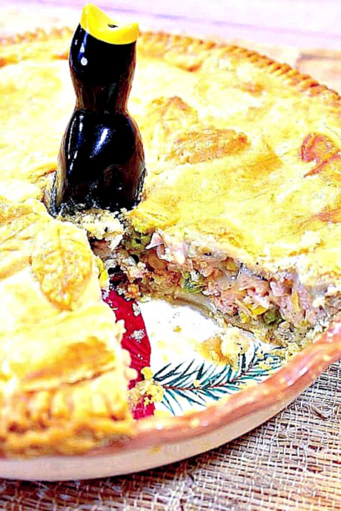 Closeup vertical photo of a pork pot pie with a slice taken out and a pie bird in the center.