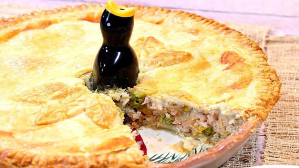 A closeup horizontal photo of a pork pot pie with a slice taken out and a pie bird on top
