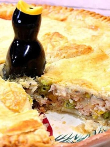 A closeup horizontal photo of a pork pot pie with a slice taken out and a pie bird on top