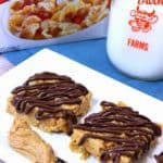 A vertical closeup photo of tiger paws cereal bars with a chocolate drizzle and a knife with peanut butter