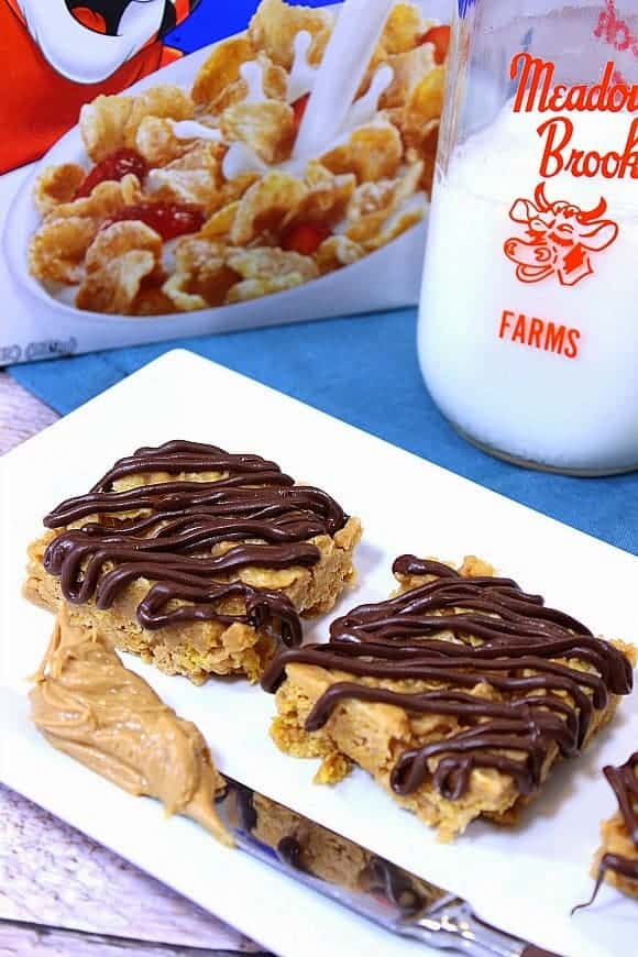 A vertical closeup image of tiger paws cereal bars on a white plate with a milk bottle and cereal box in the background.