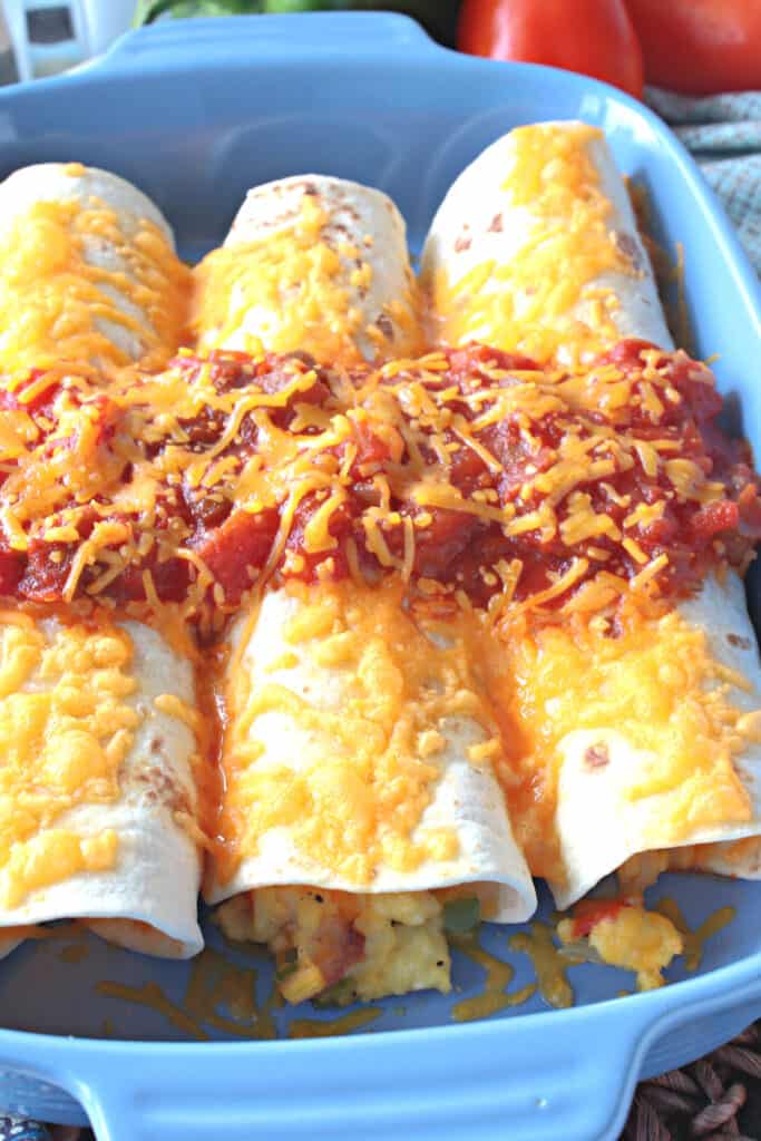 A vertical closeup overhead photo of three air fryer breakfast burritos side by side with salsa and melted cheese.