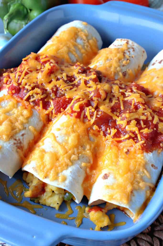 An overhead vertical image of a blue casserole dish filled with air fryer breakfast burritos with cheese and salsa.