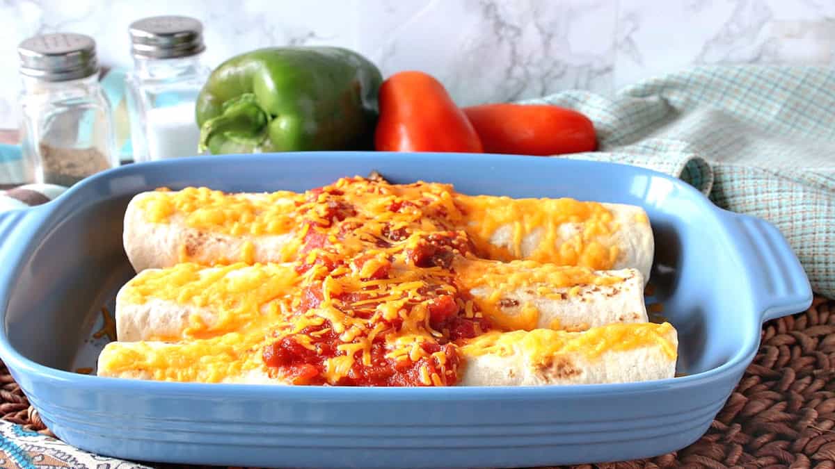 Three air fryer breakfast burritos with melted cheese and salsa in a blue casserole dish.