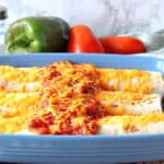 Three air fryer breakfast burritos in a blue casserole dish with salsa and melted cheese