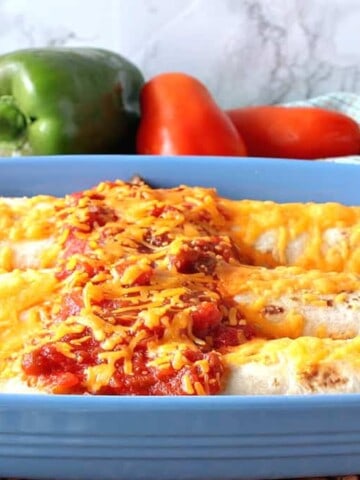 Three air fryer breakfast burritos in a blue casserole dish with salsa and melted cheese