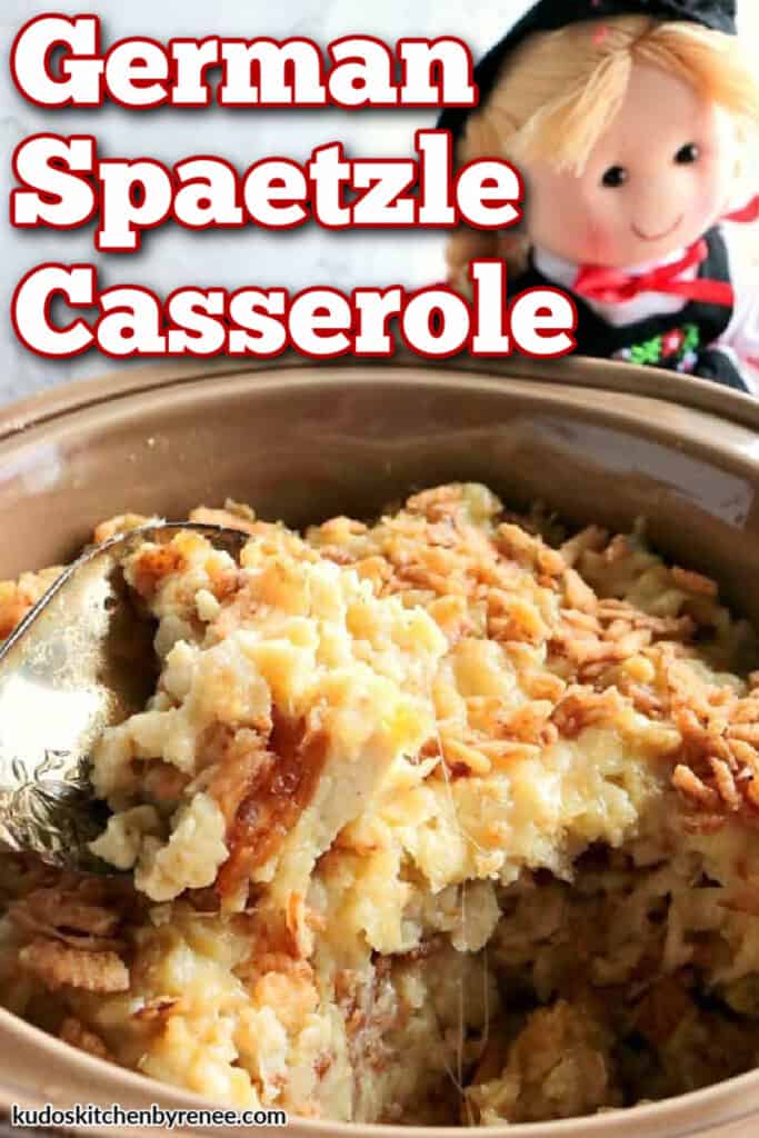 A vertical closeup image of a tan dish filled with German Spaetzle Casserole and a cute little German doll in the background.