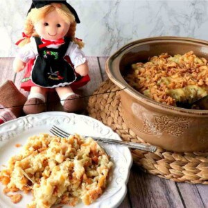 A plate of German Spaetzle Casserole in the foreground with a German doll in the background.