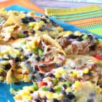 A colorful photo with loaded pulled pork nachos on a blue platter with a lime green and orange napkin in the background