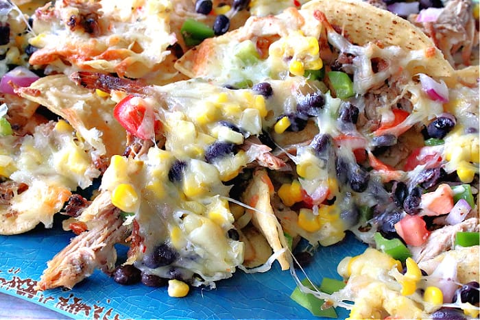 A super closeup photo of colorful Loaded Pulled Pork Nachos with melted cheese, corn, black beans, tomatoes, and green pepper.