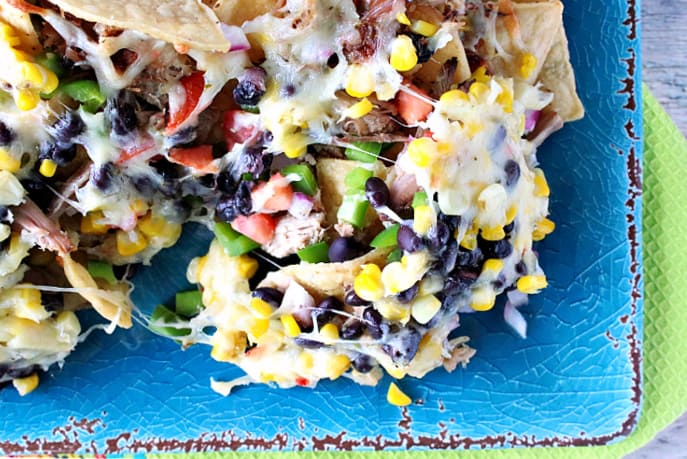 A closeup overhead photo of Loaded Pulled Pork Nachos on a blue platter with a green napkin underneath