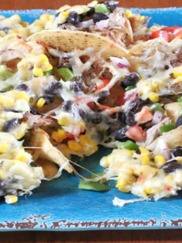 A blue platter filled with Loaded Pulled Pork Nachos with melted cheese, corn, and black beans